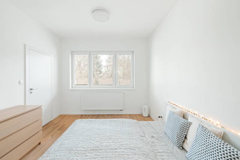 A bright bedroom in a 4-room apartment with wood-patterned flooring and decorative pillows.