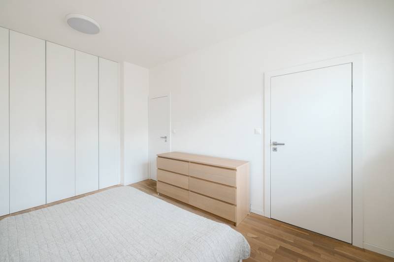 A bedroom in a 4-room apartment with white walls and a wooden decor floor.