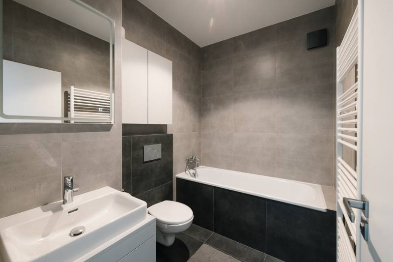 Bathroom with a bathtub, sink, and toilet in a 4-room apartment, stylish gray tiles.