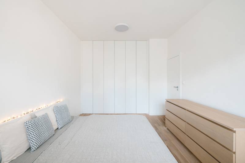 Bright bedroom in a 4-room apartment with a bed, pillows, and a wardrobe, floor with wooden decor.