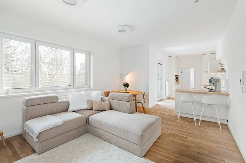 Bright living room with a kitchenette, sofa, and wooden decor flooring.