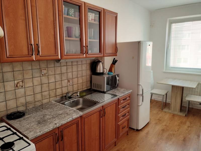 A kitchen in a 3-room apartment with a wooden decor floor and wooden furniture.