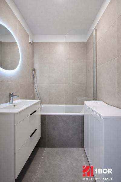 Bathroom in a 2-room apartment with a bathtub and a sink with storage space.