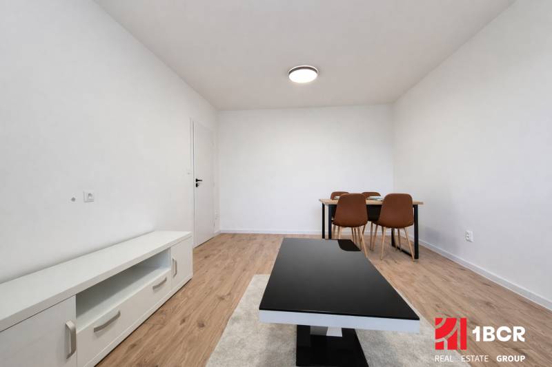 A room in a 2-room apartment with a wooden decor floor, a table, and chairs.