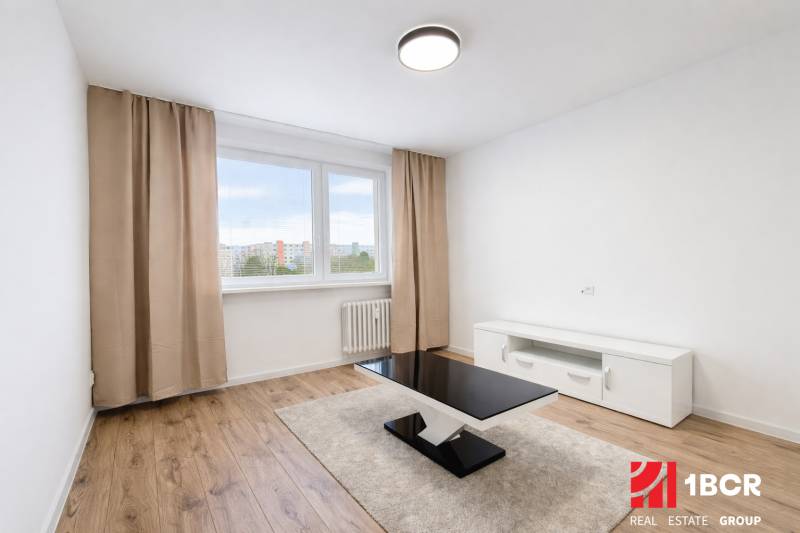 Living room with wood-patterned flooring, a table, and a white cabinet in a two-room apartment.