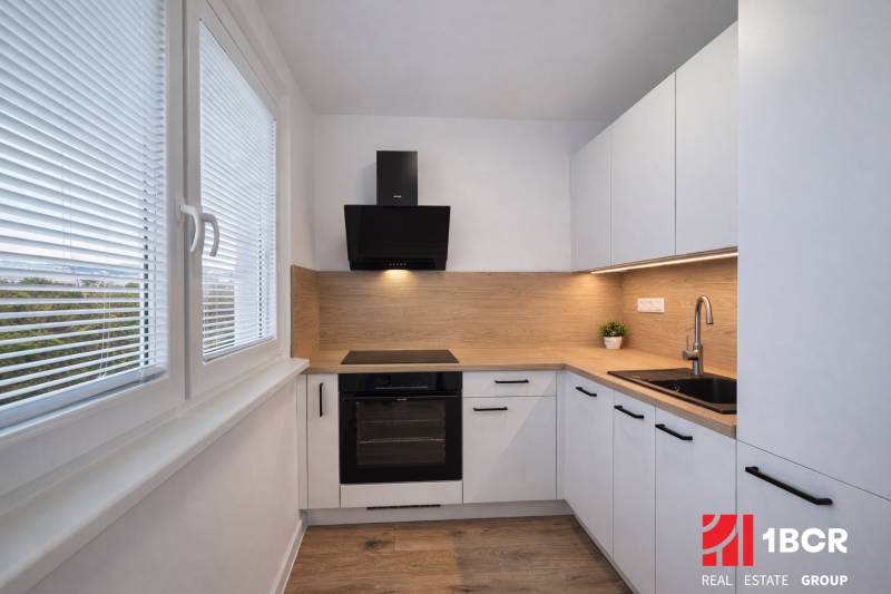 A kitchen of a two-room apartment with a wooden decor floor and white cabinets.