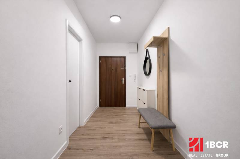 Hallway of a 2-room apartment with a wooden decor floor, mirror, and bench.