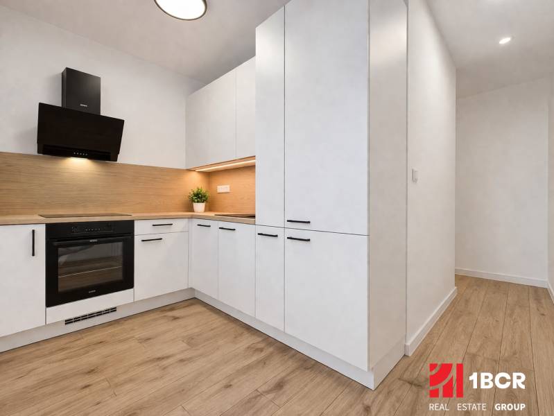 A kitchen with light furniture and a wooden decor floor in a 2-room apartment.