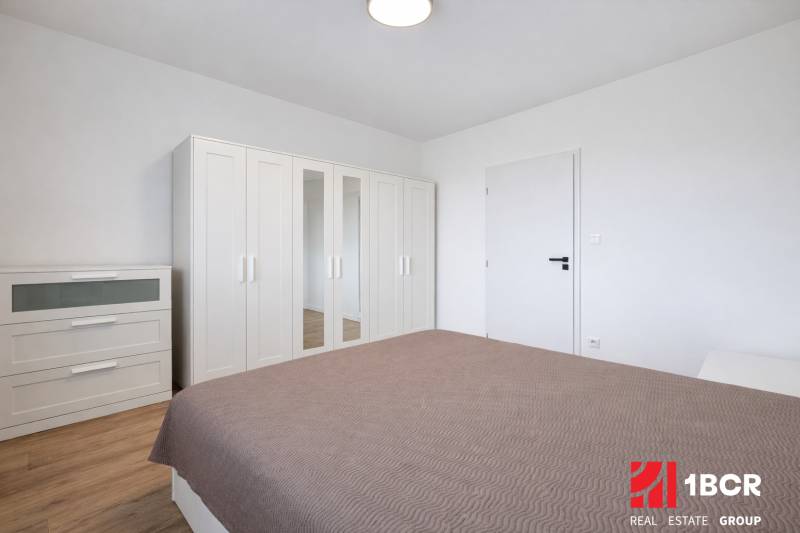 Bedroom with a white wardrobe and dresser in a 2-room apartment, floor with wooden decor.