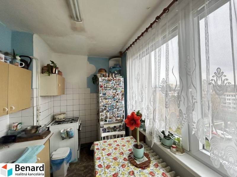 A kitchen of a three-room apartment with a large window, a curtain, and flowers on the windowsill.