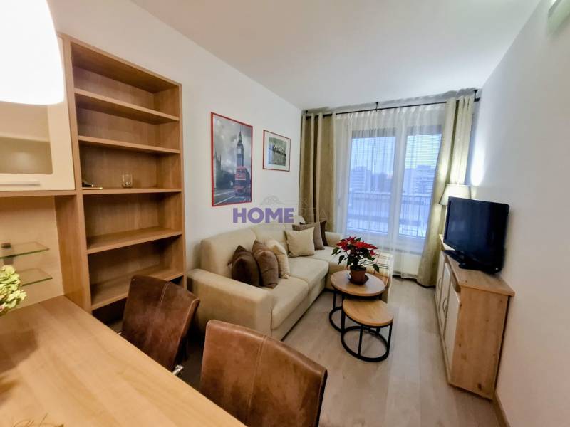 Living room in a 2-room apartment with a sofa, TV, shelves, and a wooden decor floor.