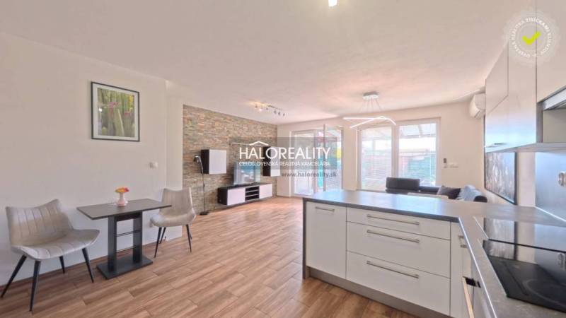 A bright living room in a two-room apartment with wood-patterned flooring and a kitchen island.