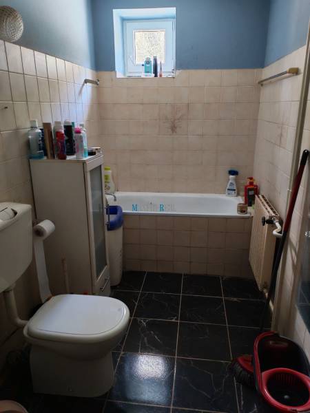 Bathroom with a bathtub and toilet in a family house, with dark tiles and a window.