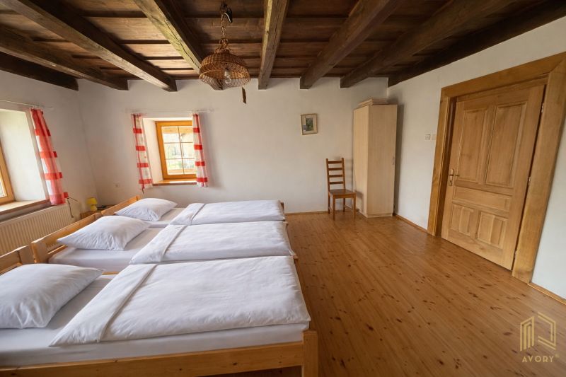 A room in a family house with a wooden ceiling, three beds, and a floor with a wooden decor.