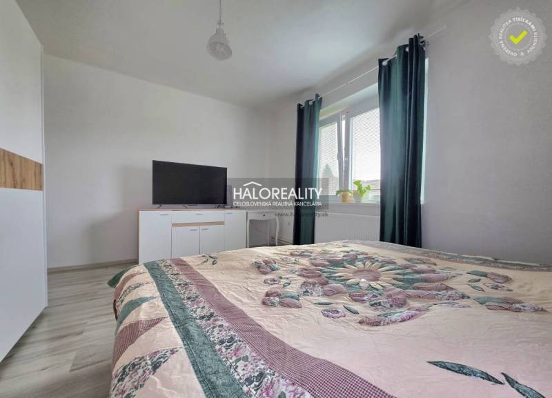 A bedroom in a family house with a bed, a television, and a window with dark curtains.