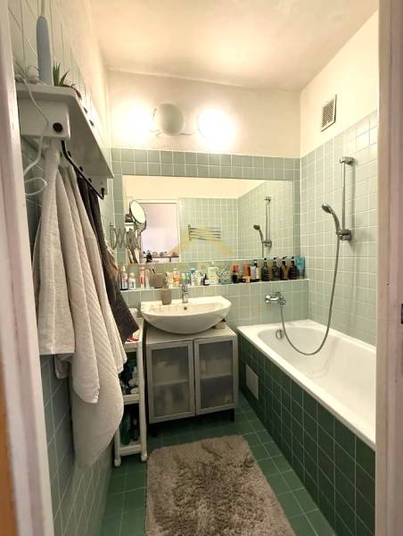 Bathroom in a 3-room apartment with a bathtub, sink, green tiles, and shelves.