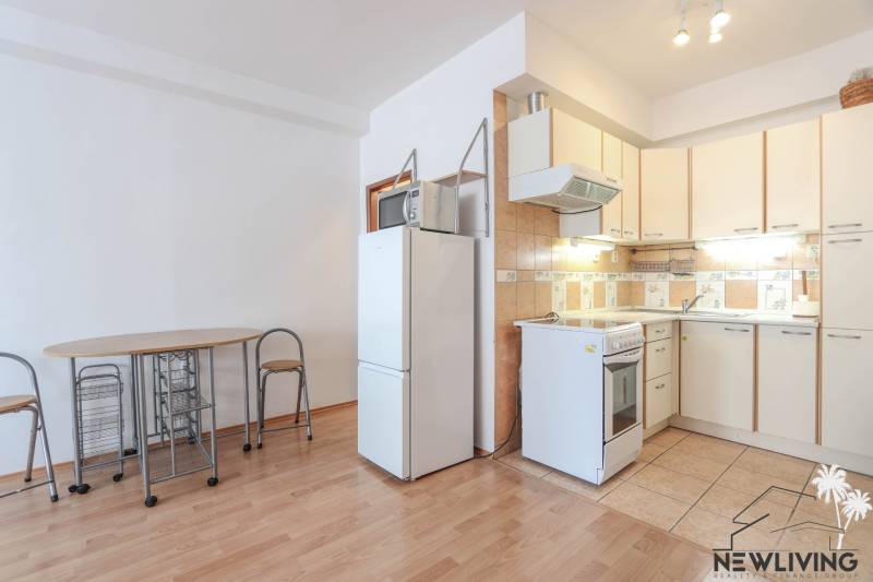 A kitchen in a 2-room apartment with a wood-patterned floor, a dining table, and a refrigerator.