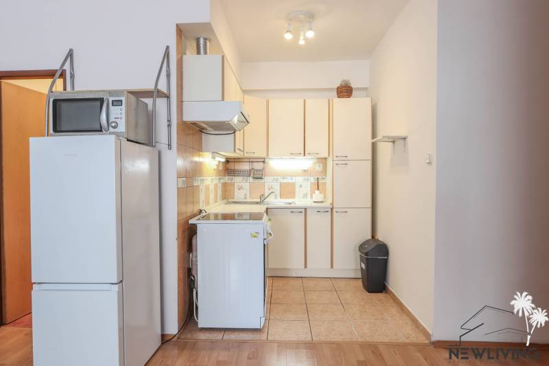 Kitchen unit with a refrigerator and microwave in a 2-room apartment, floor with wooden decor.