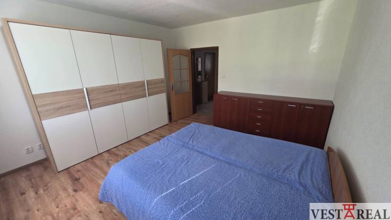 A bedroom in a studio apartment with wood-patterned flooring and practical furniture.