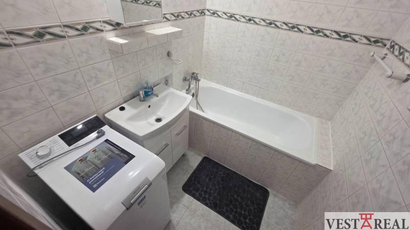 Bathroom with a bathtub and a washing machine in a studio apartment, light tiles and storage space.