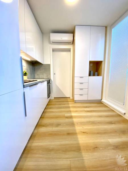 A kitchen with white cabinets and a wood-patterned floor in a two-room apartment.