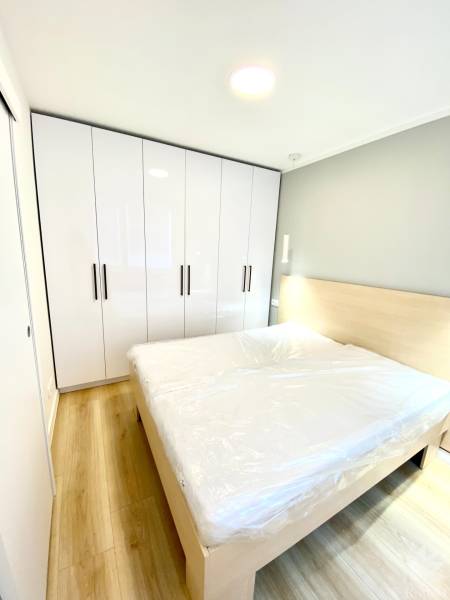 Bedroom with a double bed, white wardrobe, and wooden decor flooring in a two-room apartment.