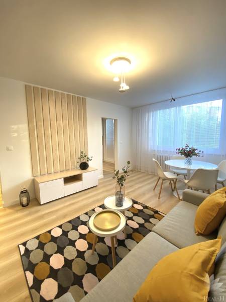 Living room of a two-room apartment with a wood-patterned floor, light furniture, and decorations.