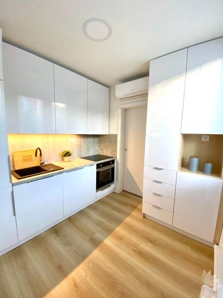A kitchen in a 2-room apartment with white cabinets and a wood-patterned floor.