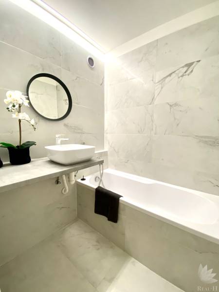 A bathroom in a 2-room apartment with a bathtub, a mirror, and floral decoration.