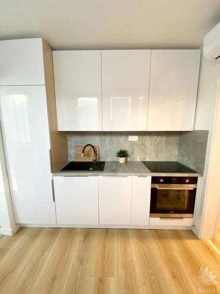 A kitchen unit with white cabinets, a gray countertop, and a floor with a wood decor, 2-room apartment.