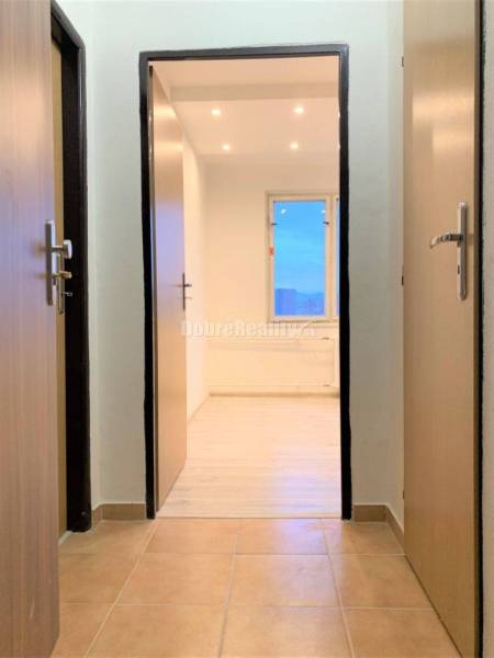 A hallway with ceramic tiles and an entrance to a room with a wooden decor floor.
