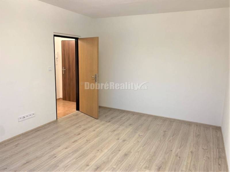 A room in a one-room apartment with white walls and a wooden decor floor.