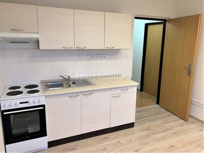 Kitchen unit with an electric stove, white cabinets, and a wooden decor floor in a studio apartment.