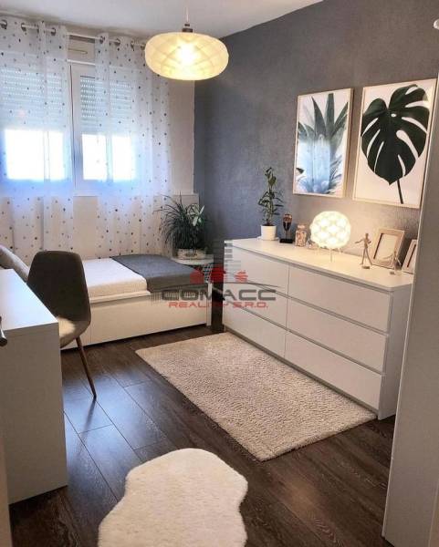 A room in a family house with a wooden decor floor, artistic paintings, and decorative flowers.