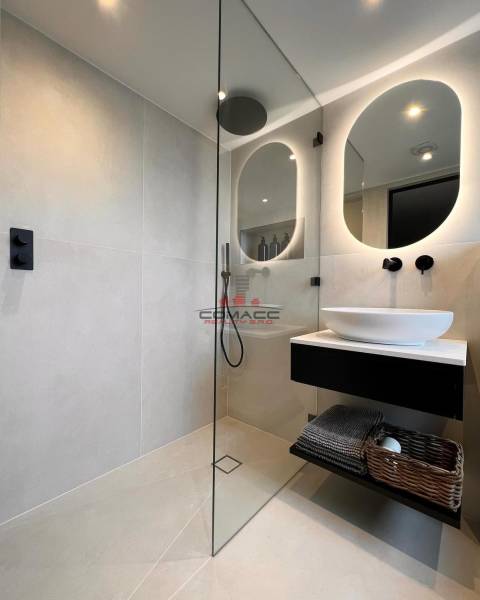 A bathroom in a family house with an illuminated mirror, a glass shower enclosure, and a sink.
