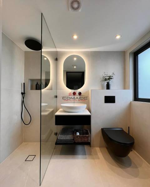 A bathroom in a family house with an oval mirror, a sink, and a black shower enclosure.