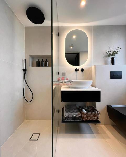 A bathroom in a family house with an illuminated mirror, black accessories, and a shower.