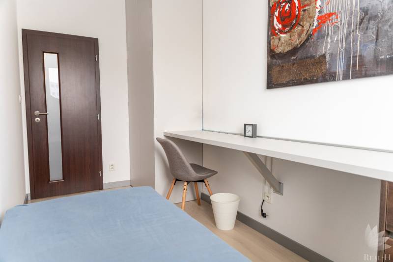 A room in a 4-room apartment with a wooden decor floor, a table, and a chair.