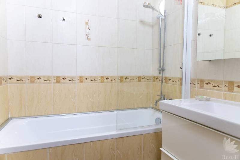 Bathroom with tiles and a bathtub in a 4-room apartment, light colors and a shower head.