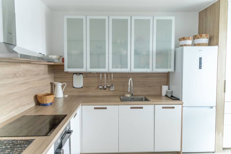A kitchen in a 4-room apartment with a wooden decor floor and white cabinets.