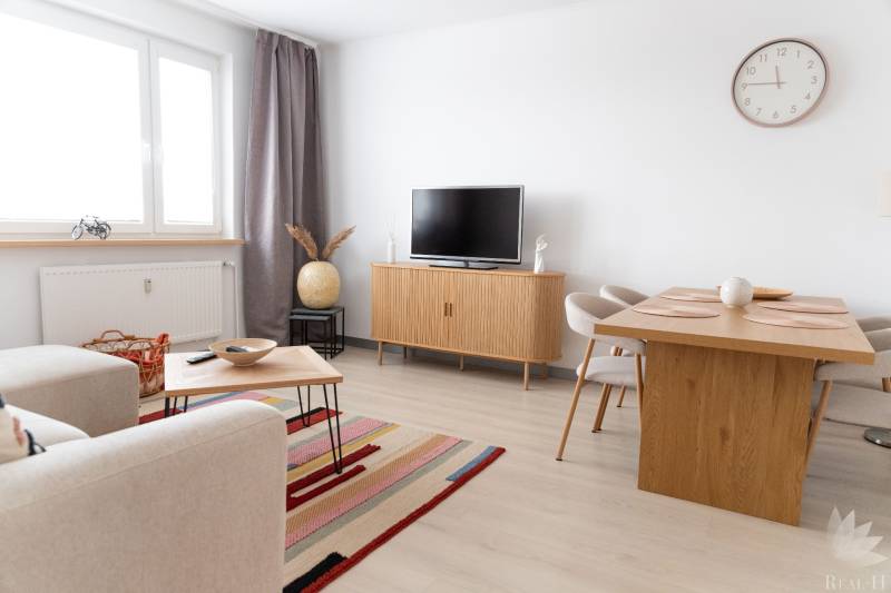 Living area of a 4-room apartment with a TV, sofa, table, and floor with wooden decor.
