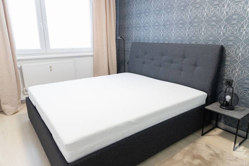 A bedroom with a gray bed, patterned wallpaper, and a nightstand.