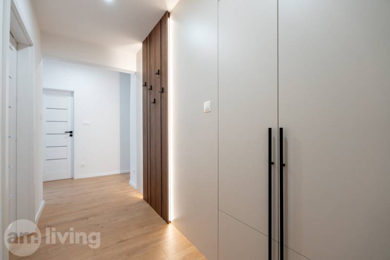 A hallway in a 3-room apartment with a light-colored wall and a wood-patterned floor.