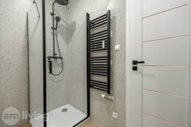 Shower enclosure with a black shower set and a heating ladder in a 3-room apartment.
