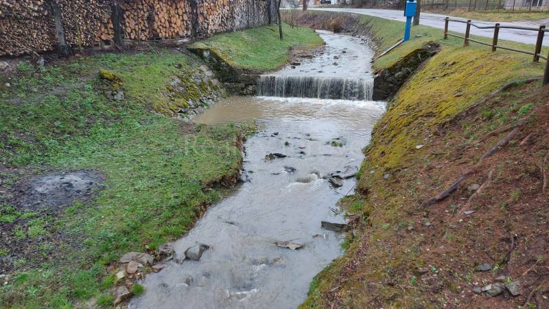 A stream flowing through recreational lands in Púchov with wood stored on the edge.