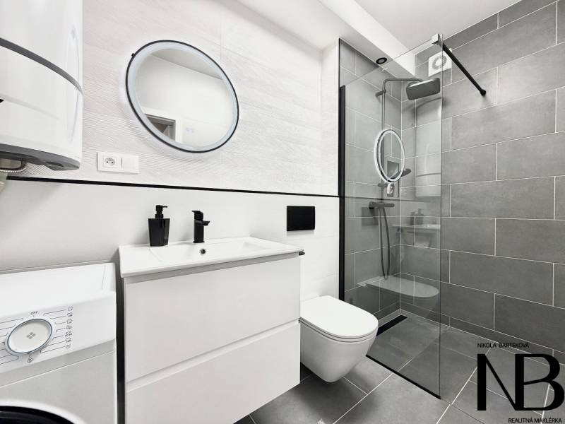 A bathroom in a studio apartment with modern grey tiles and a glass shower enclosure.