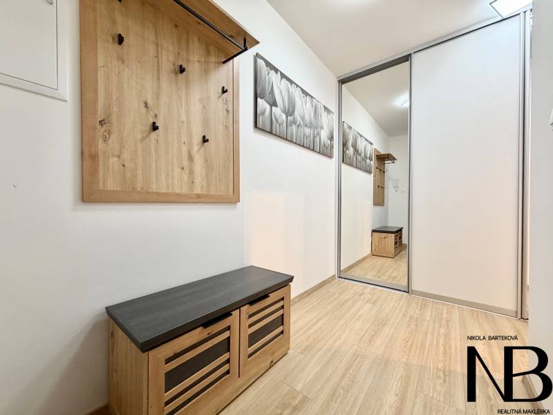 A hallway of a one-room apartment with a coat rack and a floor with a wooden decor.