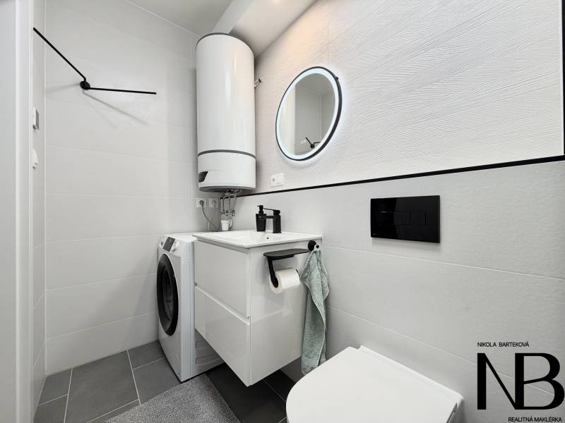 A bathroom in a one-room apartment with a washing machine, boiler, and a mirror in a circular frame.