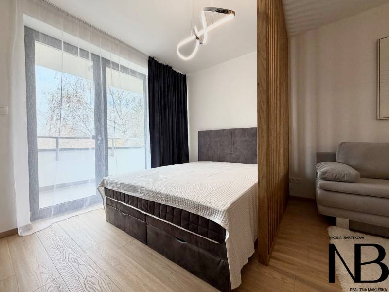 Bedroom in a studio apartment with a bed, sofa, and wood-patterned flooring.