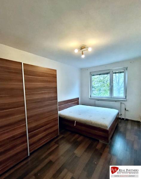 A bedroom with a wardrobe, bed, and wooden decor flooring in a 4-room apartment.